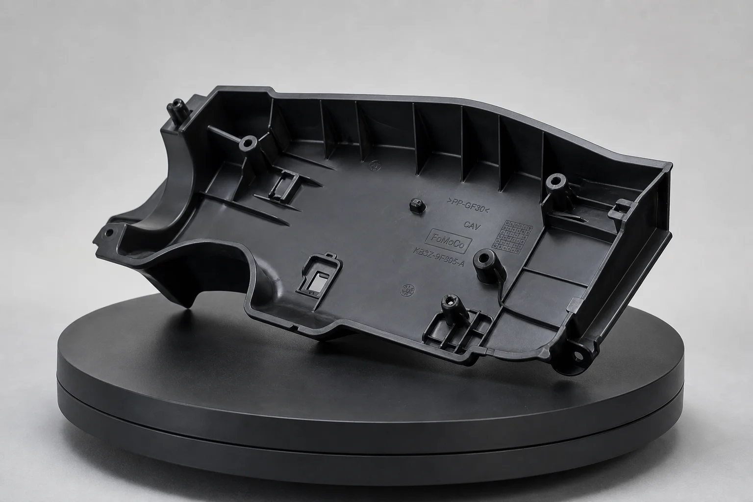 Schwarzes Kunststoff-Automobilteil mit tiefen Taschen und geprägtem Text auf einem Drehteller