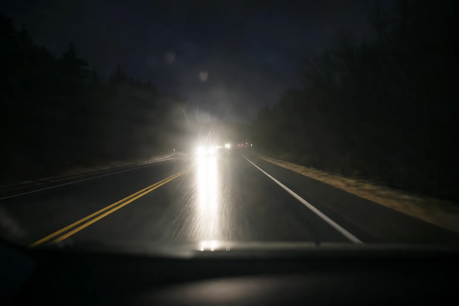 Night driving scene with oncoming headlights and wet road surface
