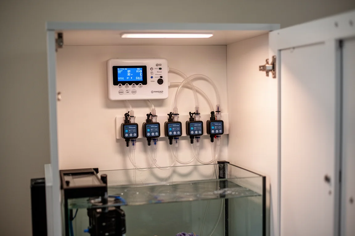Interior del mueble de un acuario de arrecife con controladores montados en una fila ordenada sobre un panel de pared
