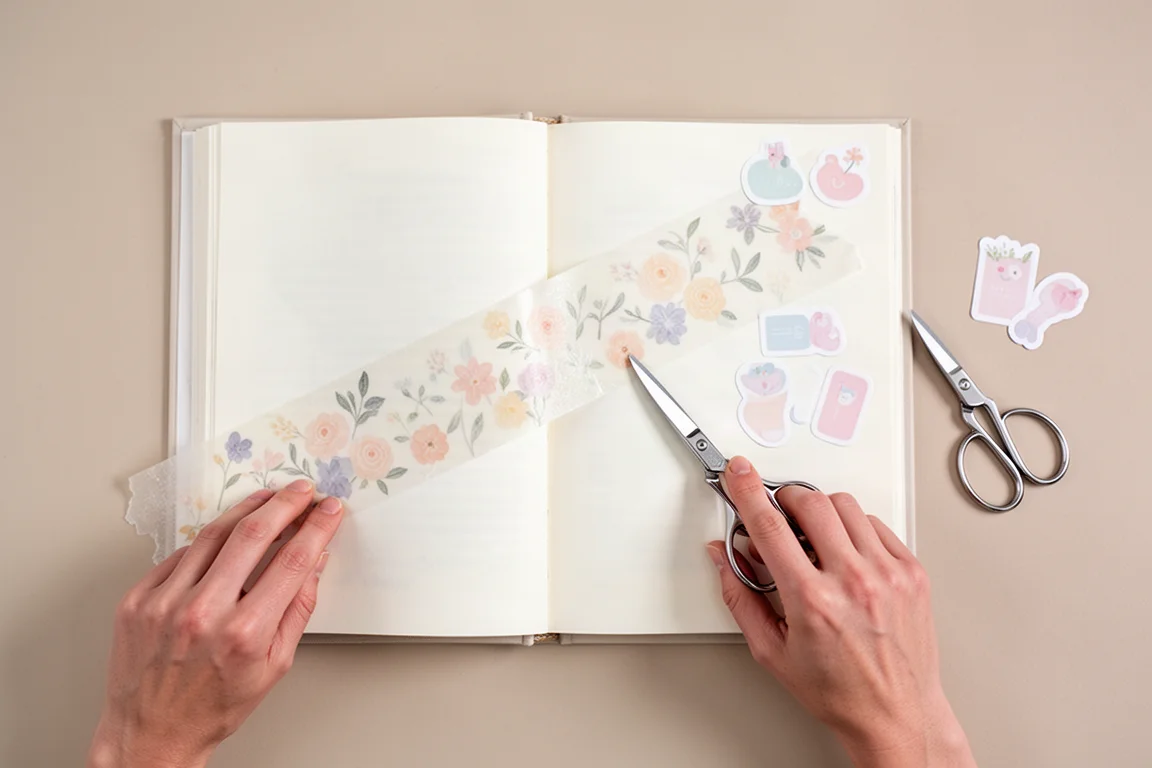 Dłonie nakładające przezroczystą taśmę i naklejki na stronę Bullet Journala
