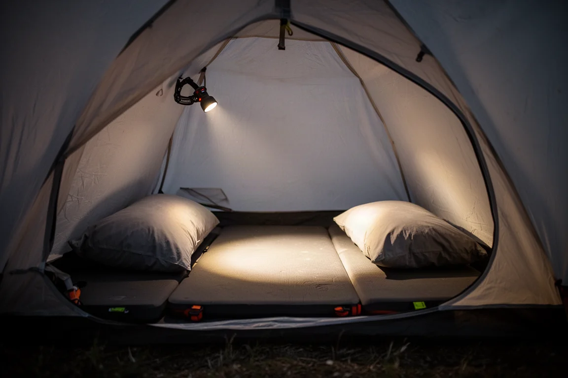 Interior of a small tent at night with sleeping pad, pillow, and warm headlamp glow