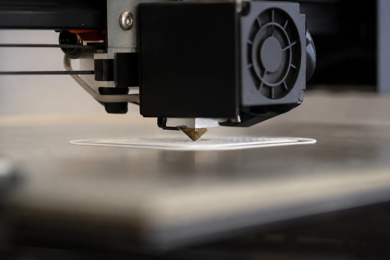 3D printer nozzle extruding white PLA filament onto heated build plate