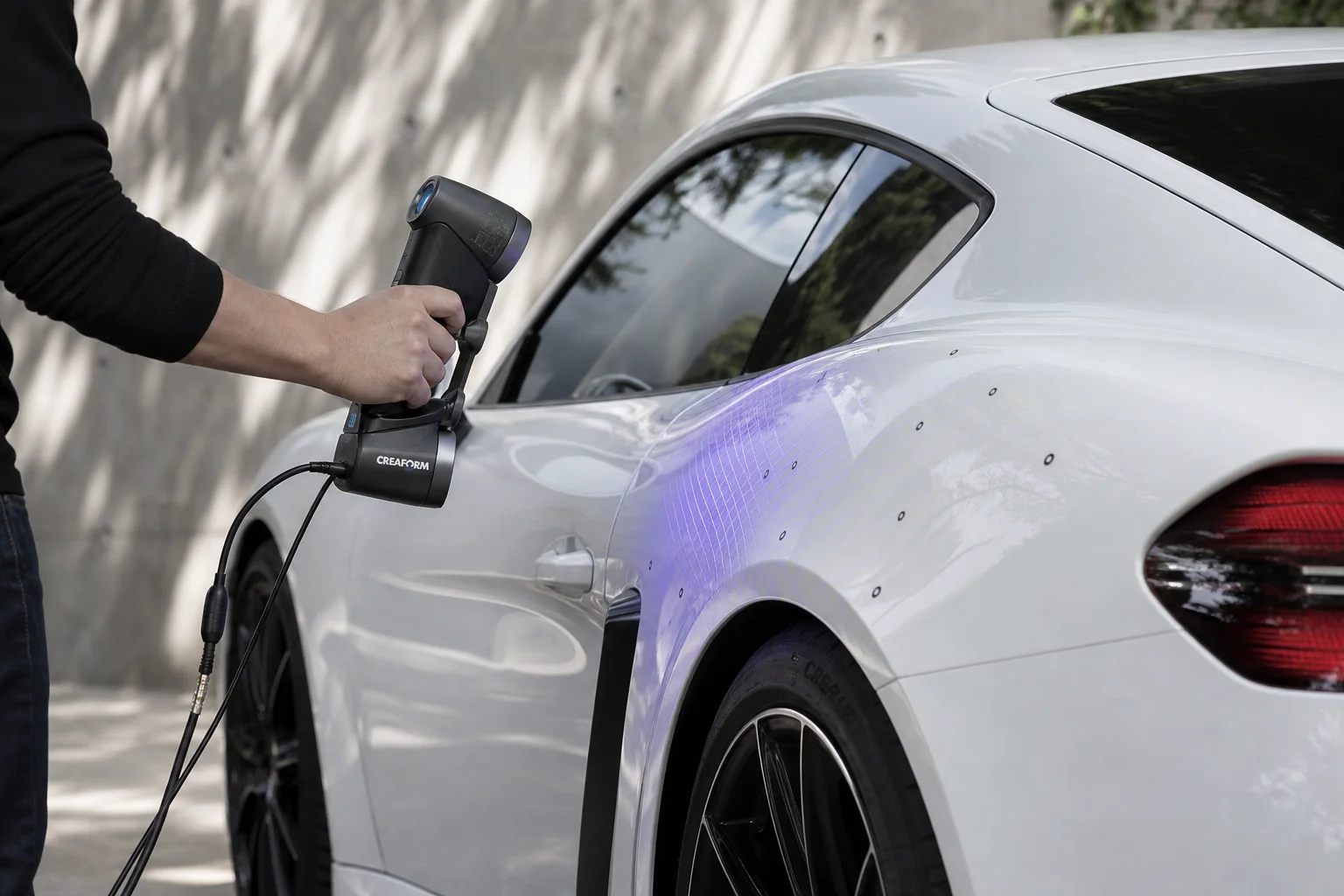 Technician scanning a vehicle exterior with a handheld 3D scanner outdoors