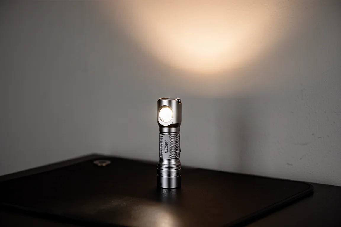 鈦金屬機身電筒以尾蓋直立於深色表面上,散發溫暖光暈