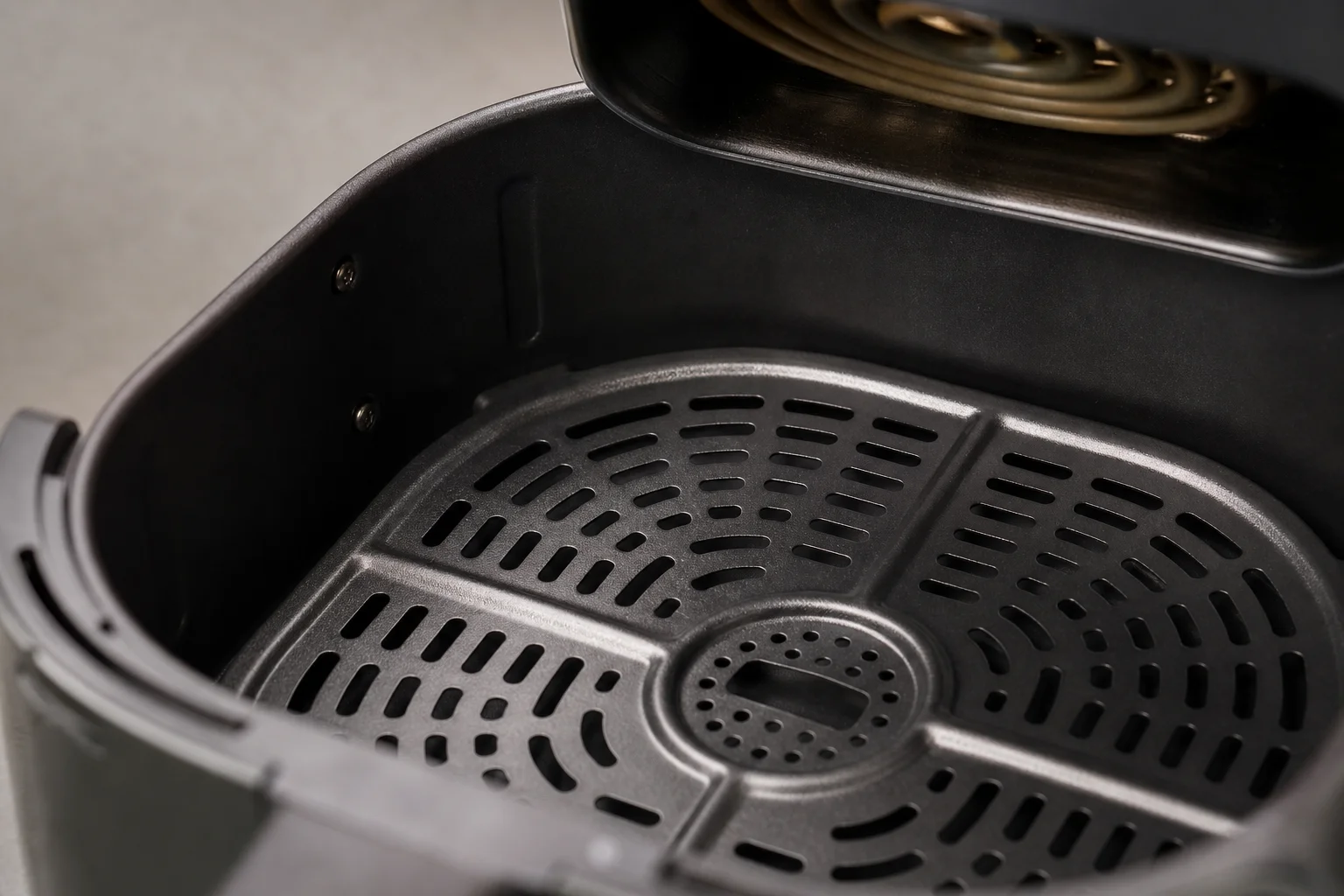 Gros plan sur l'intérieur du panier d'une friteuse sans huile montrant la surface perforée et l'élément chauffant