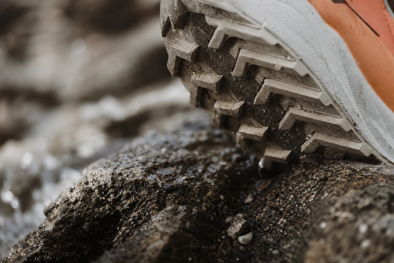 Primo piano della suola di una scarpa da trail con tasselli di trazione su una superficie rocciosa bagnata