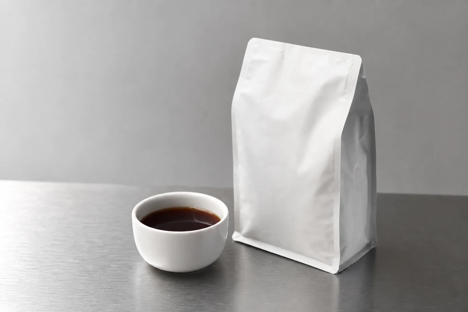 A coffee cup and bag in soft studio lighting on aluminium surface