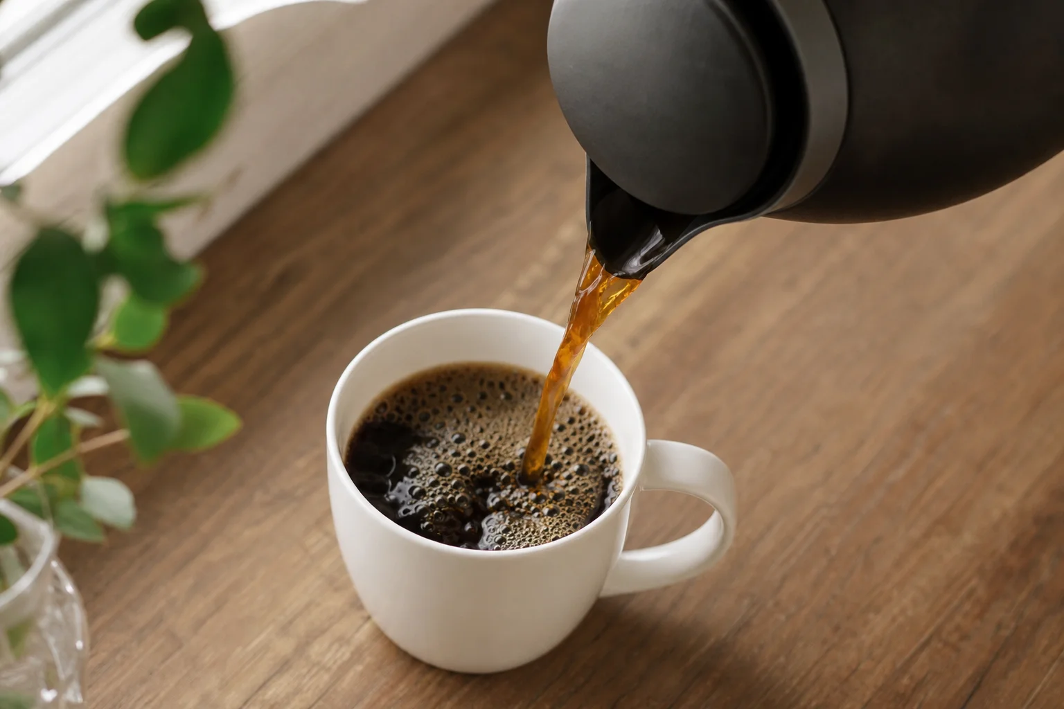 Vertiendo café preparado de una jarra térmica en una taza de cerámica blanca