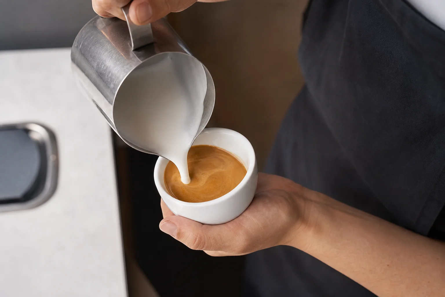 Barista pouring steamed milk into espresso for latte art