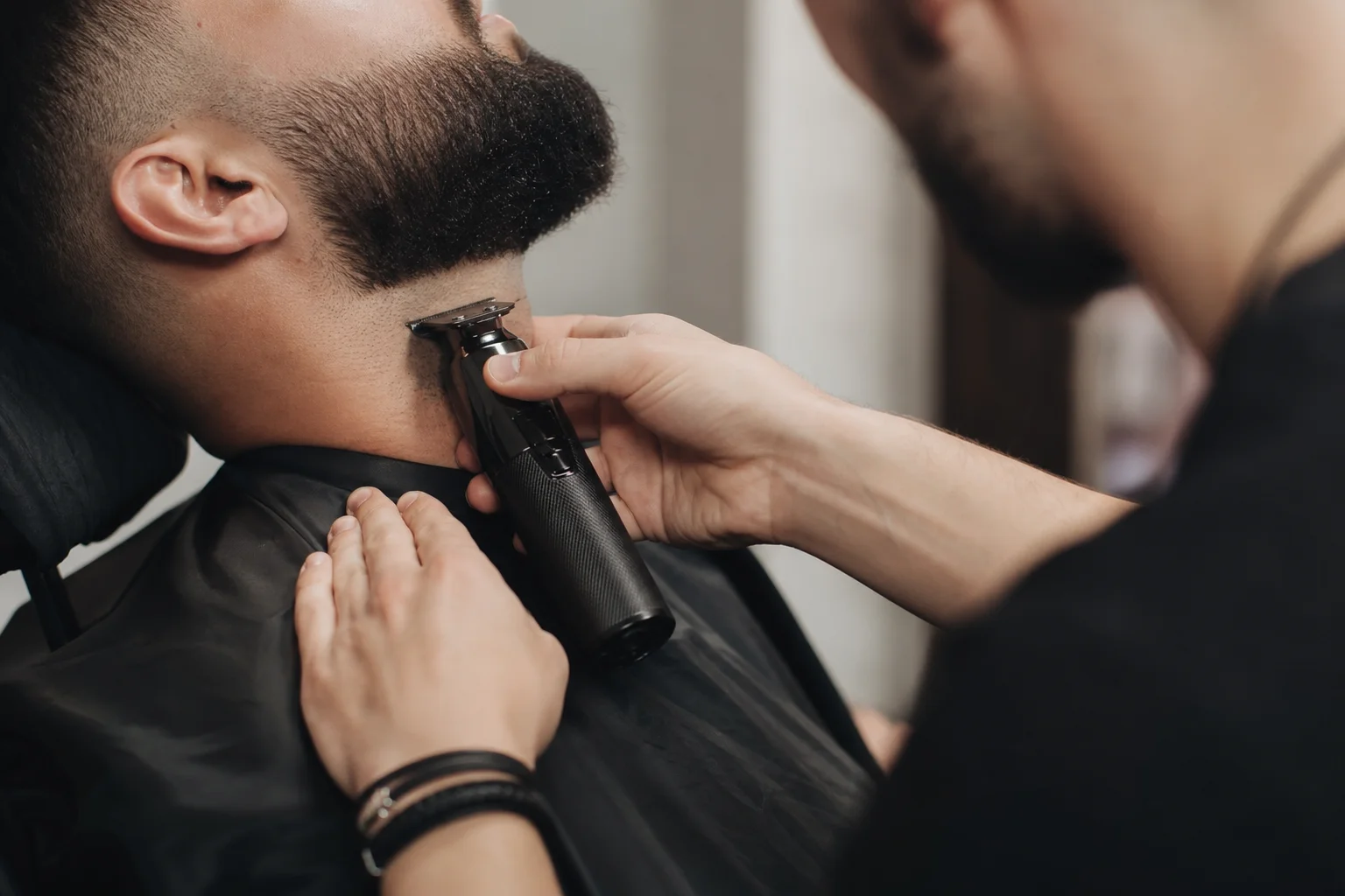 Barbier effectuant des finitions détaillées au niveau du cou et des joues avec une tondeuse haute vitesse