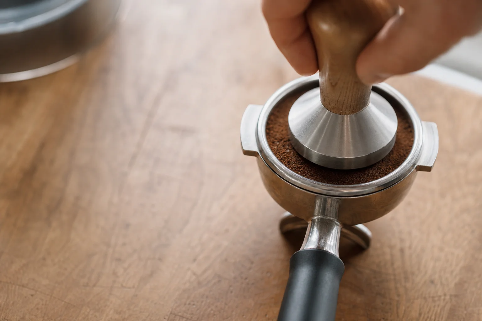 Stainless steel portafilter with grounds being tamped on wooden counter