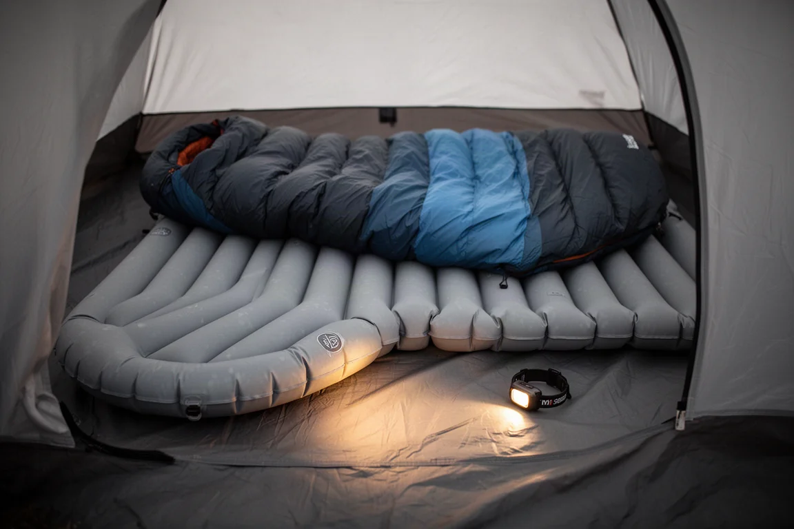 Opgeblazen slaapmat en slaapzak uitgespreid in een tent met de gloed van een hoofdlamp