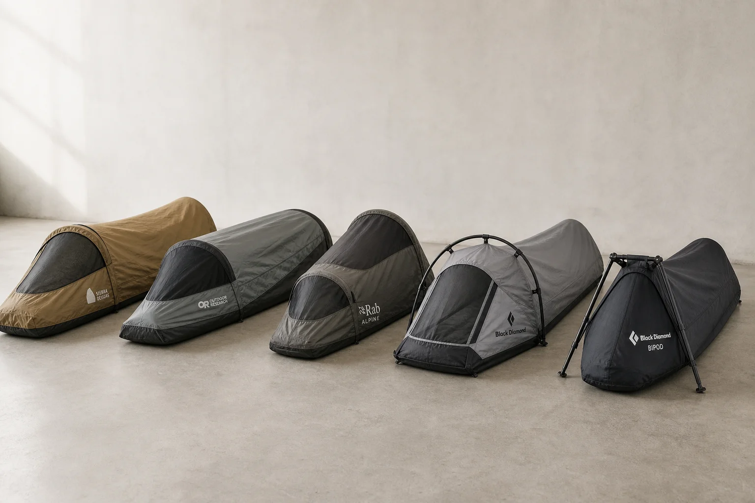 Cinque bivvy bag disposti in fila su una superficie in cemento, che mostrano design e colori differenti