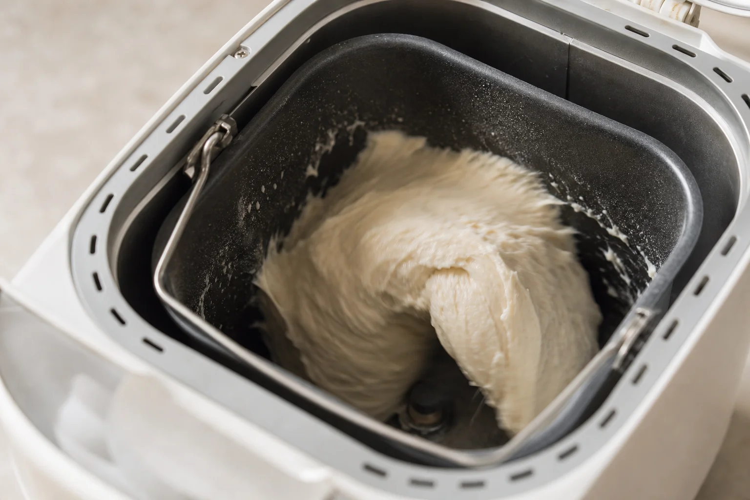 Hände beim Kneten von Teig in einem Brotbackautomaten mit sichtbarem Mischvorgang