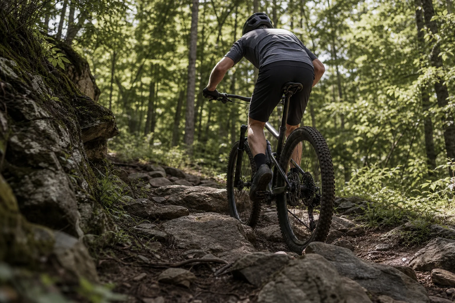 Mountainbiker fährt auf einem felsigen Trail mit grünem Waldhintergrund bergauf