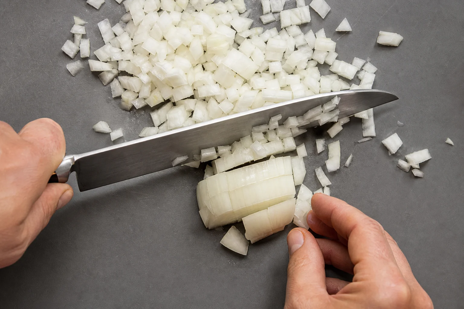 Couteau de chef coupant des oignons en dés uniformes sur une planche à découper