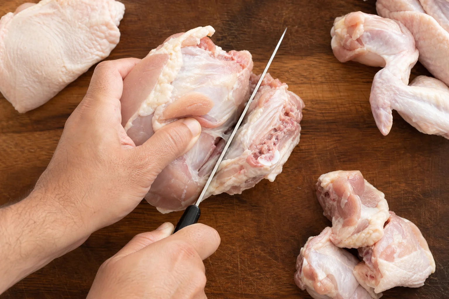 Kockkniv som skär genom rå kyckling på en skärbräda