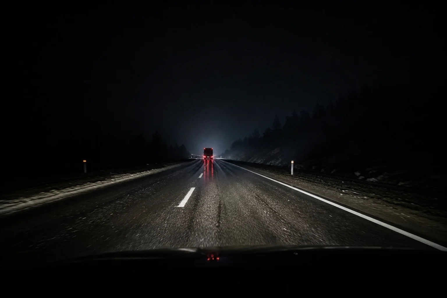 Nighttime road scene with vehicle headlights illuminating wet asphalt and distant taillights