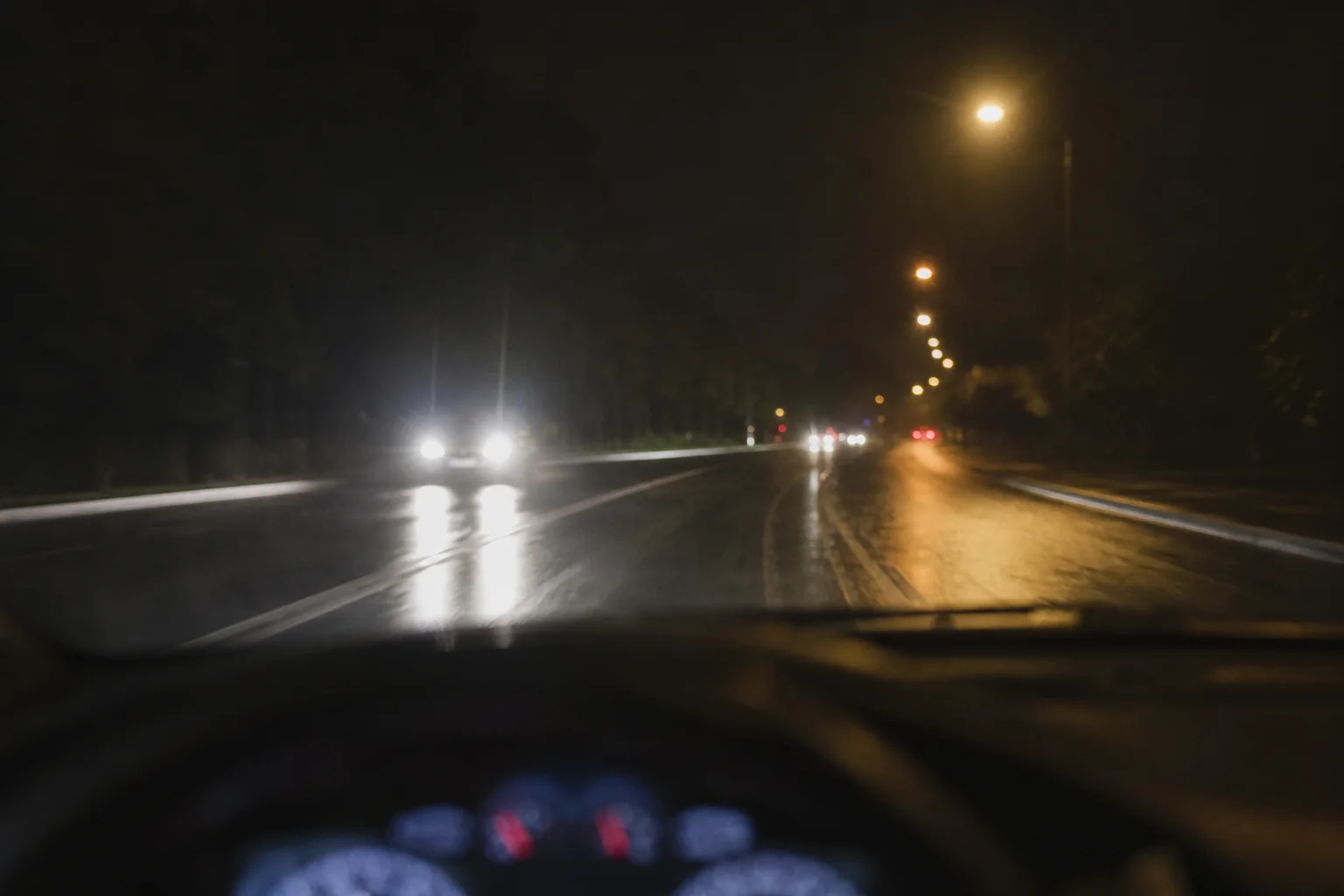 Nächtliche Fahrszene mit entgegenkommenden Scheinwerfern und Blendung durch Straßenbeleuchtung