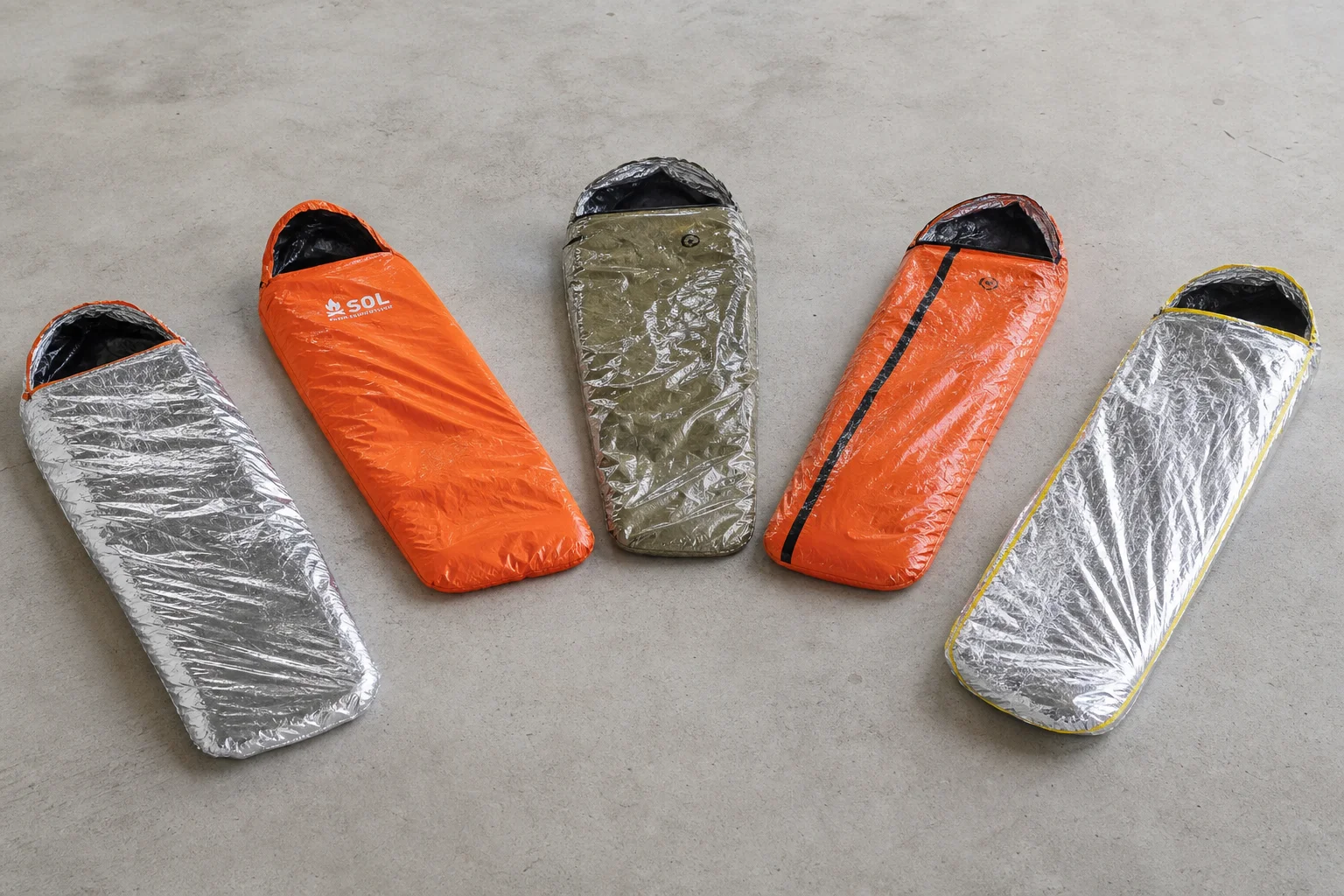 Five emergency sleeping bivys in different colors arranged on concrete surface