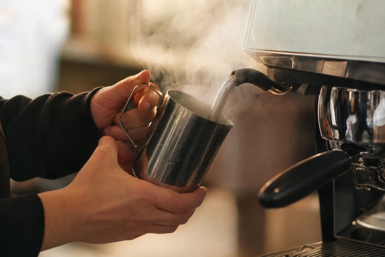 Barista steaming milk in pitcher with espresso machine steam wand