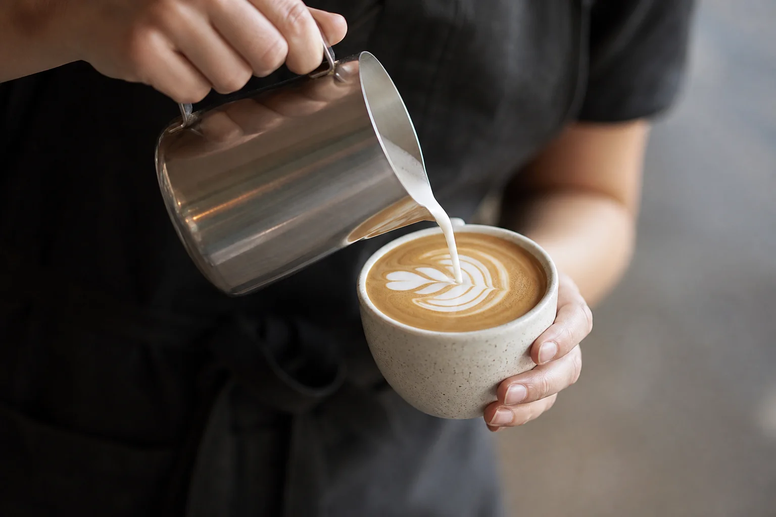 Latte art being poured into espresso cup with milk pitcher