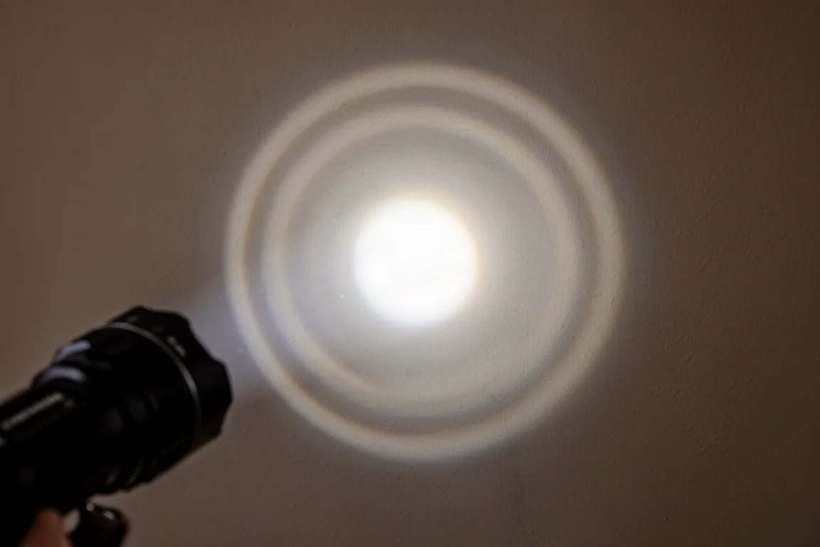 Close-up of a flashlight beam projecting onto a dark wall with visible light rings