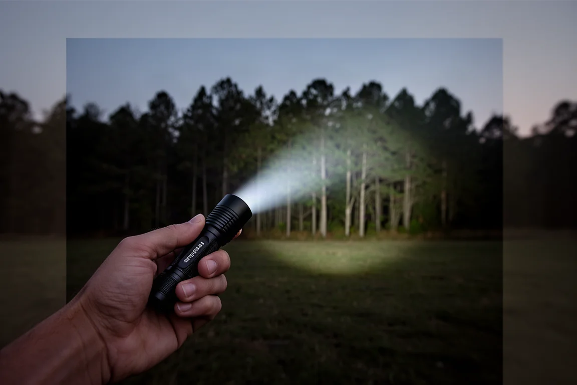 Hand holding a compact flashlight in a dark outdoor setting at dusk