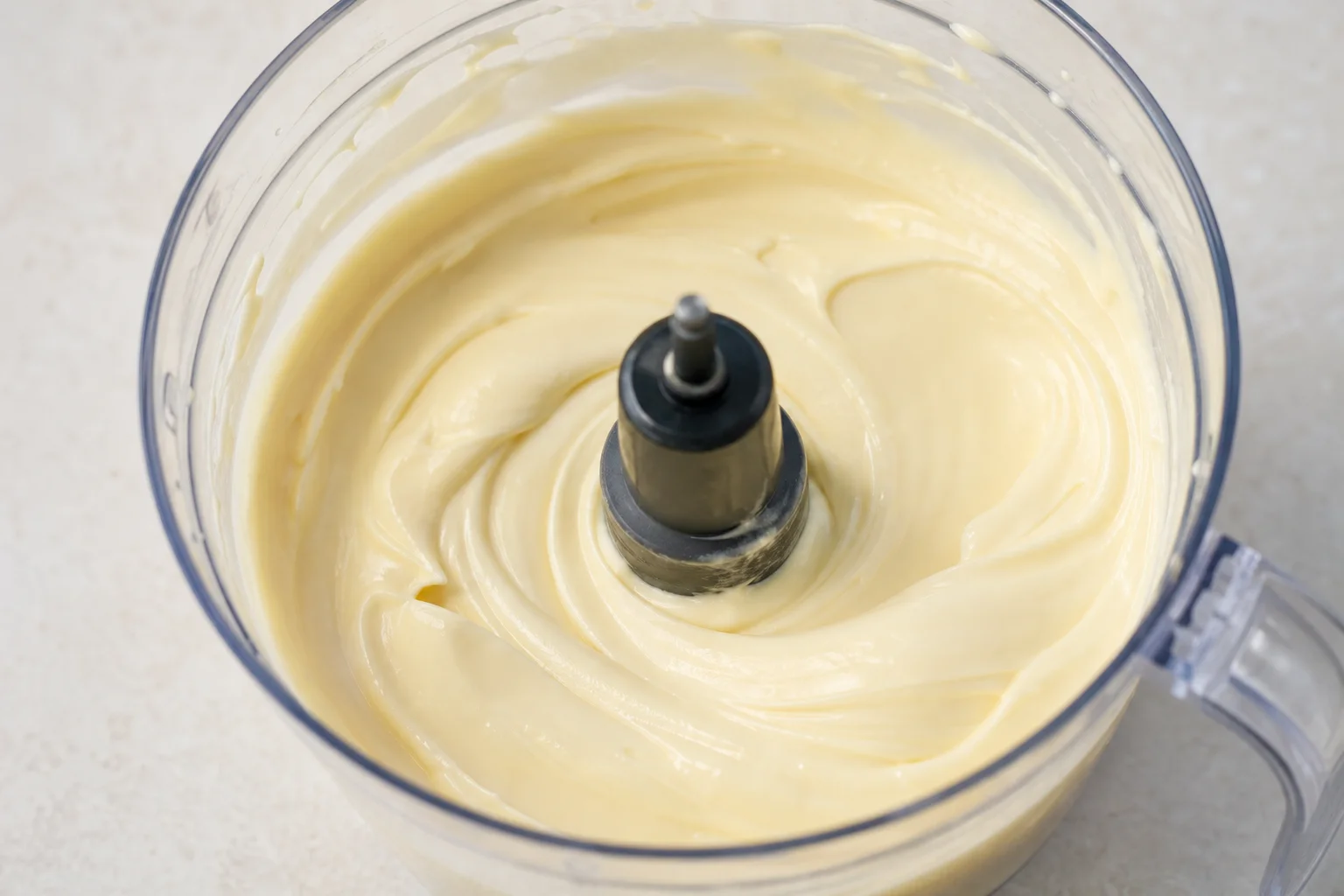 Maionese fatta in casa nel contenitore di un robot da cucina, dal colore giallo pallido e cremoso