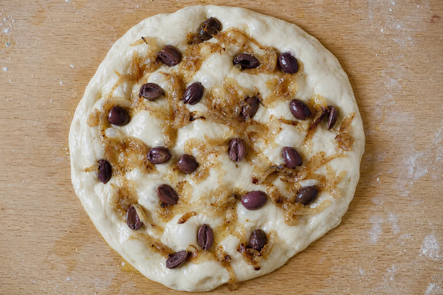 Impasto rustico per pizza con cipolle caramellate e olive su una superficie in legno
