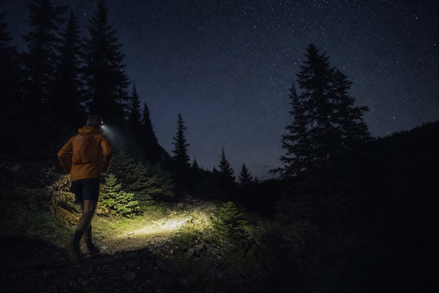 Corredor de trail con linterna frontal en un sendero forestal oscuro por la noche