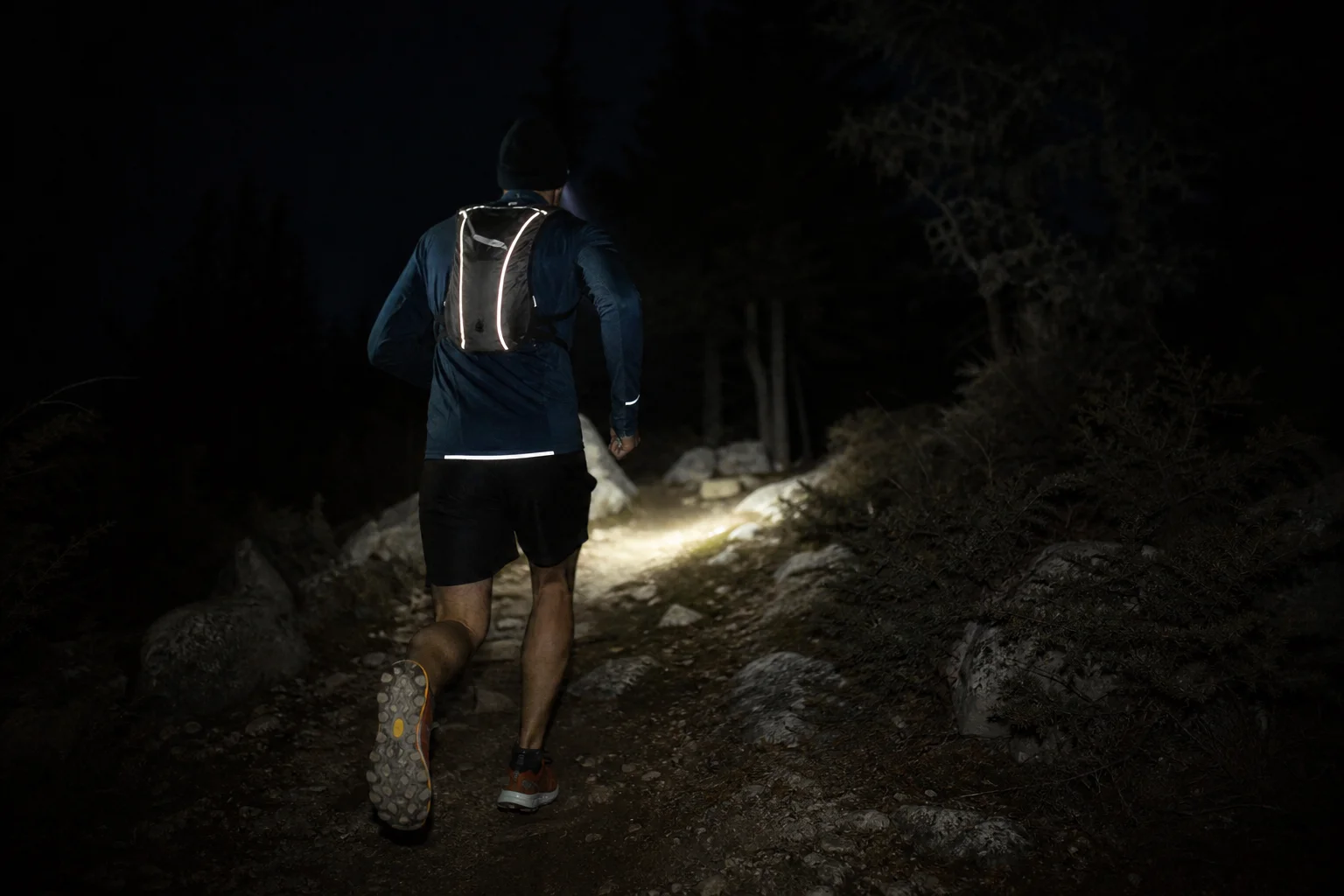 Corredor nocturno en movimiento usando una linterna frontal ligera en un sendero oscuro