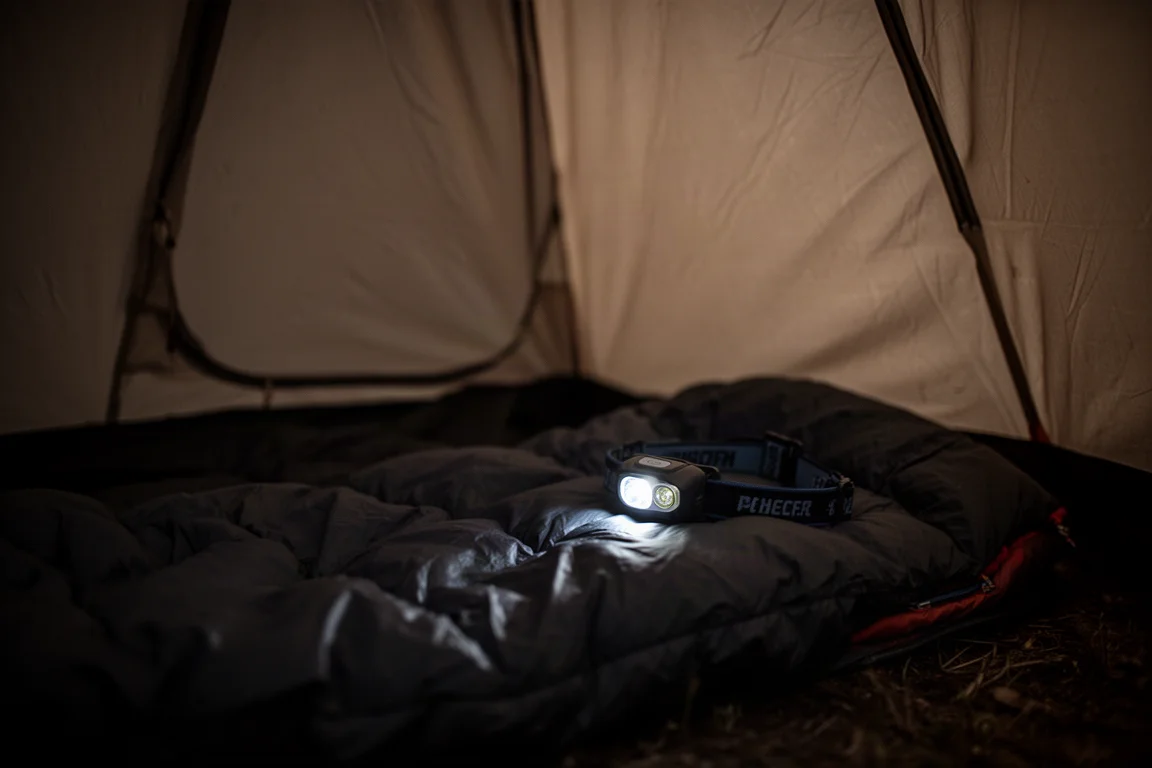 Gros plan sur une lampe frontale produisant une lumière très tamisée dans l'intérieur sombre d'une tente