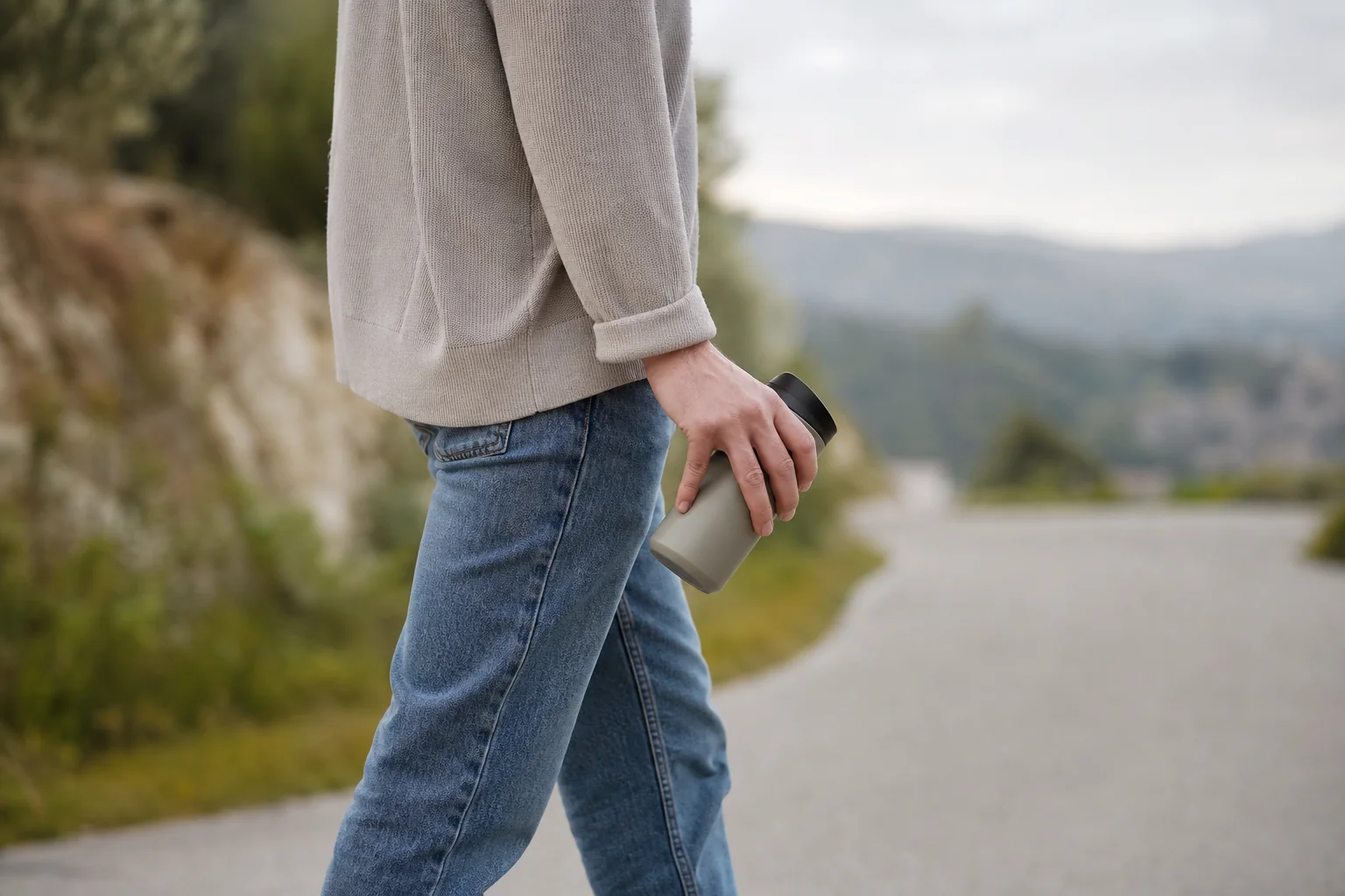 Person holding travel mug in one hand while walking outdoors