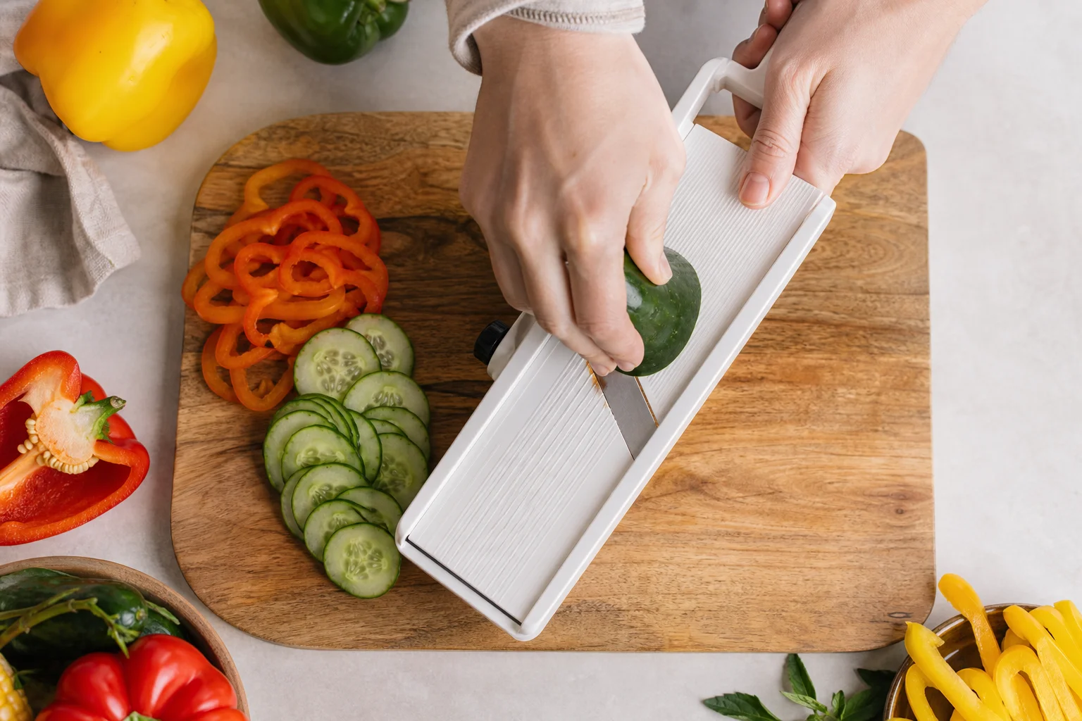Hands using a mandoline slicer to cut vegetables on a wooden cutting board