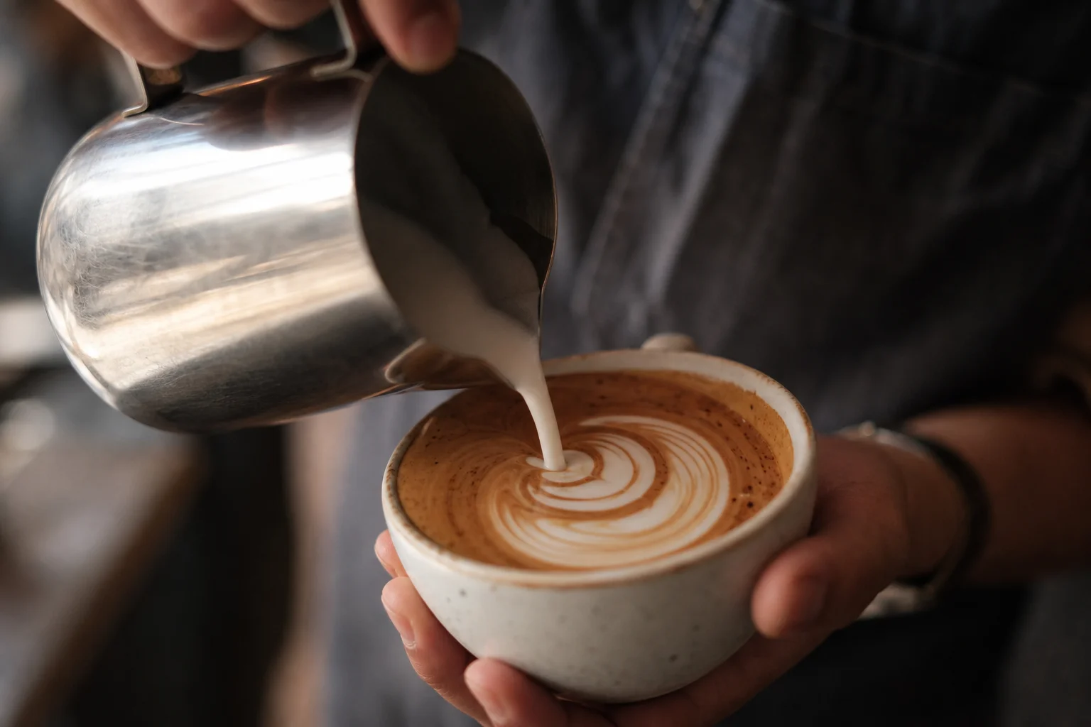 Barista pouring steamed milk into espresso to create latte art