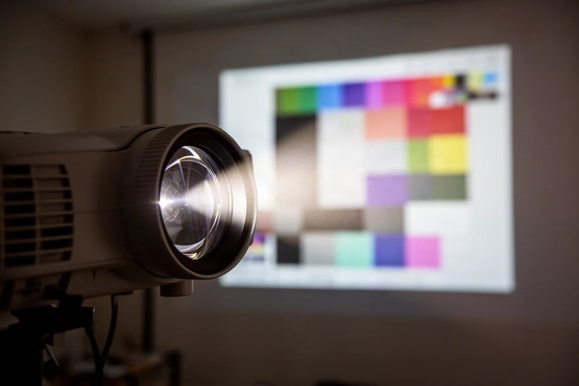 Nahaufnahme einer Projektorlinse, die ein helles Testbild auf eine Leinwand projiziert