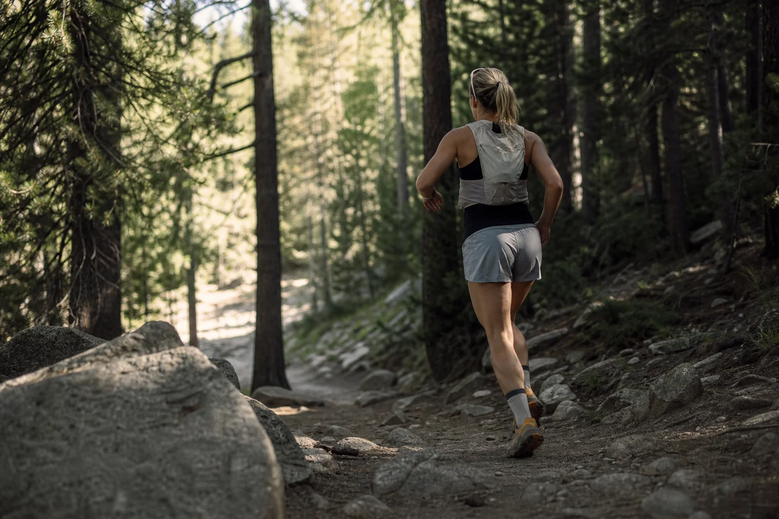Trailrunner mit Sonnenbrille auf dem Kopf auf einem schattigen Waldweg