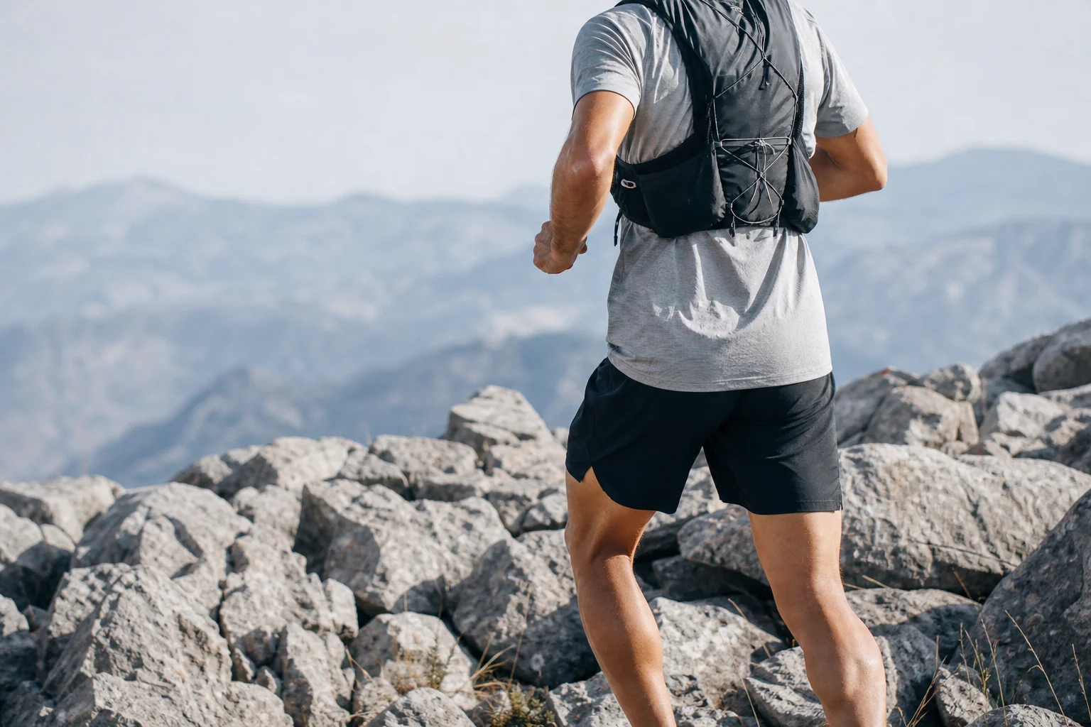 Runner su un sentiero tecnico con dettaglio della tasca rinforzata del gilet visibile