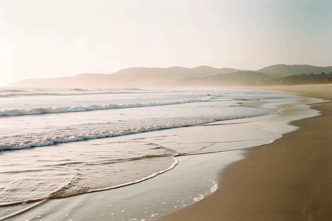 Orilla de playa de arena con olas suaves y luz tenue de atardecer