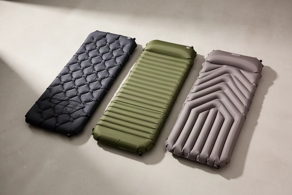 Three inflatable backpacking sleeping pads arranged side by side on a pale concrete floor
