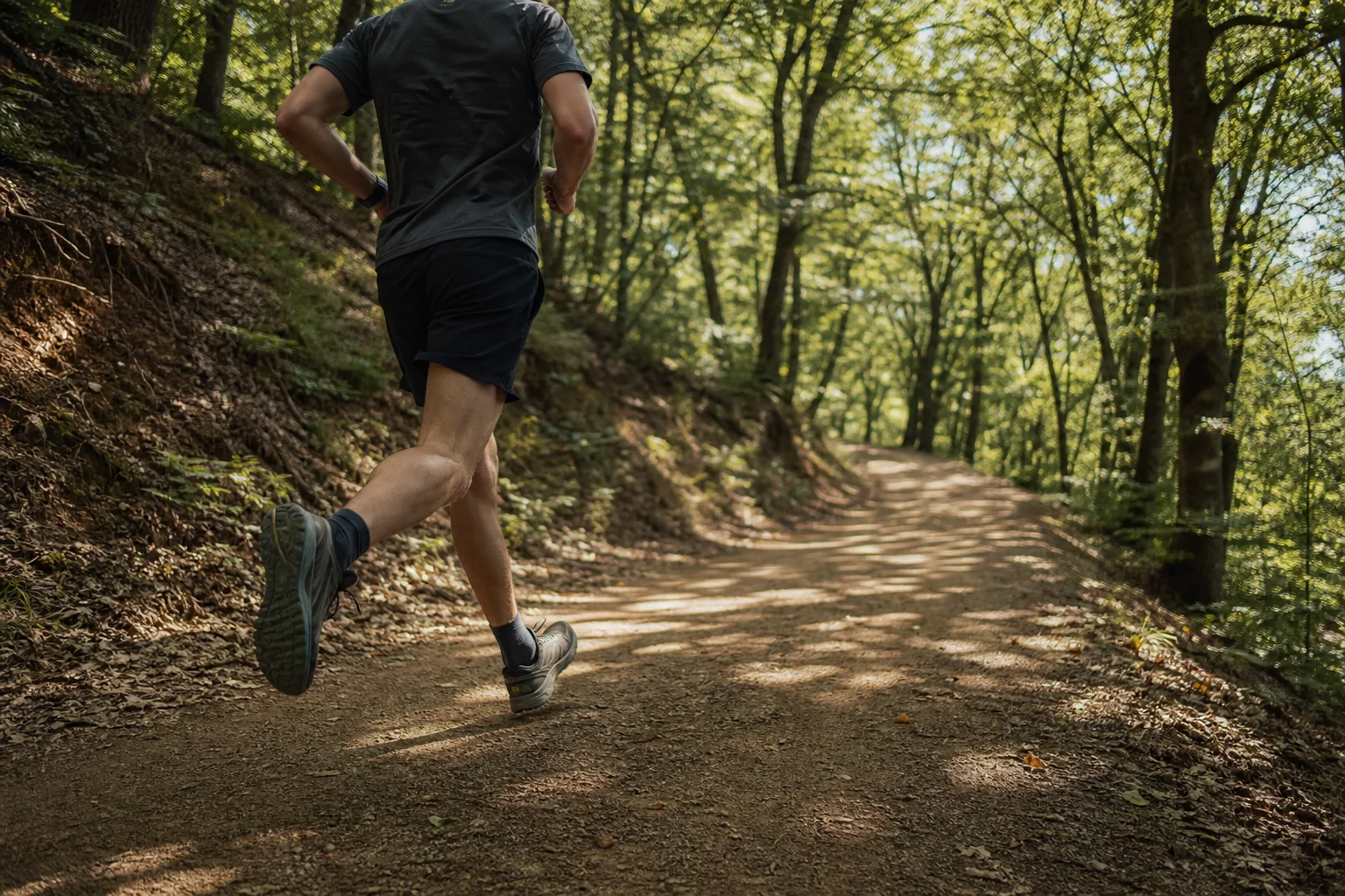 Trail runner in motion on smooth dirt path through sunlit forest