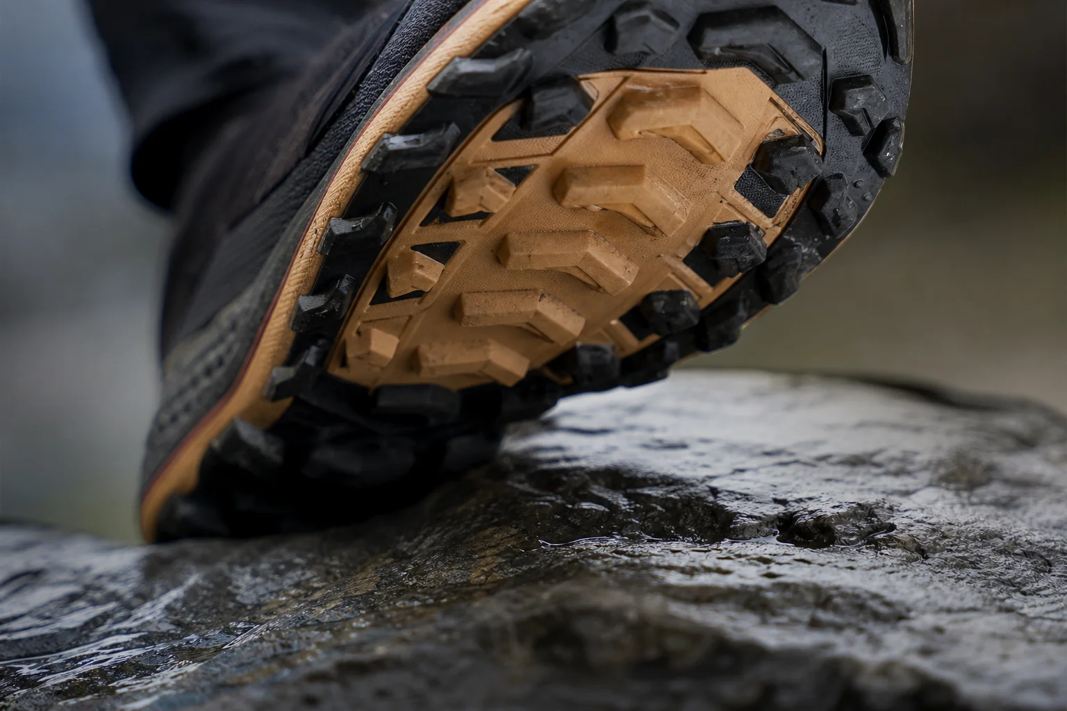 Close-up detail of a shoe sole showing grip lugs on wet rock surface