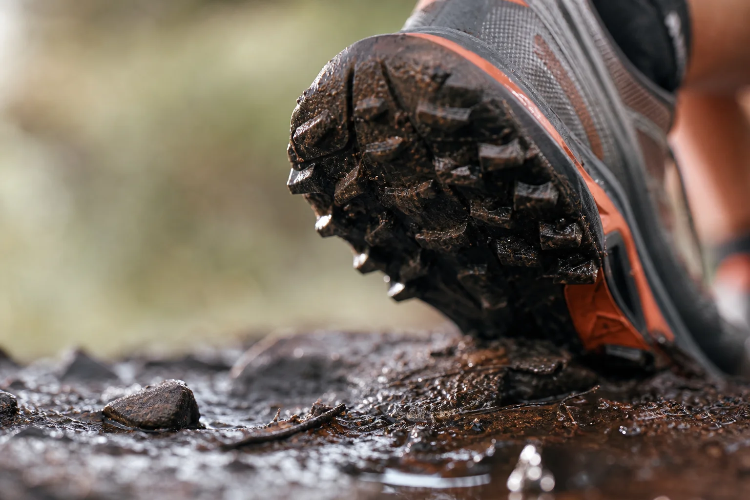 Close-up of trail shoe tread gripping wet muddy surface