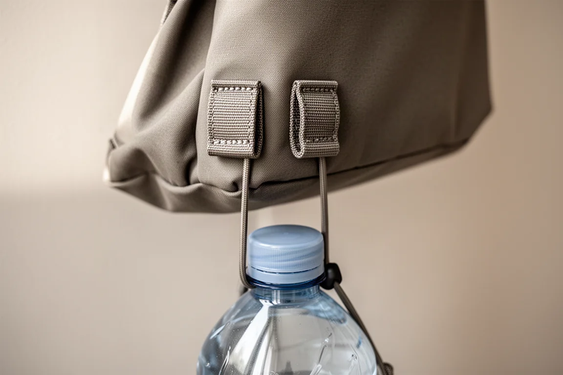 Versterkte stoflussen aan een sling bag die via een klein riempje een waterfles vasthouden