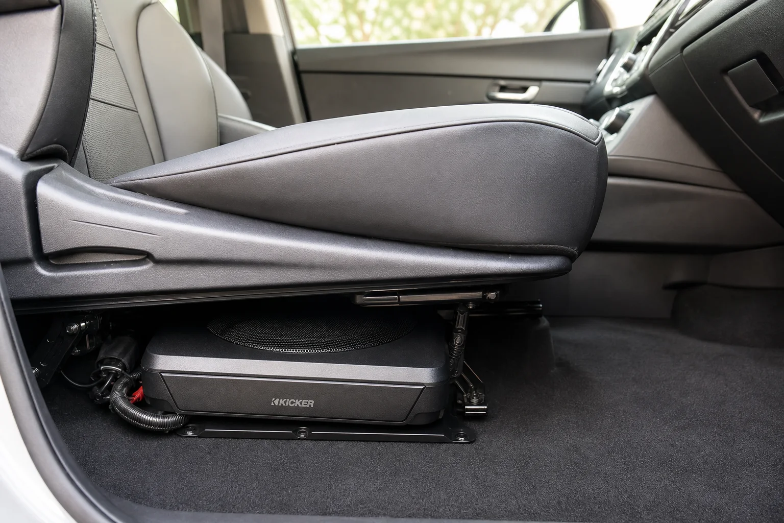 Car interior showing compact subwoofer installation under front seat