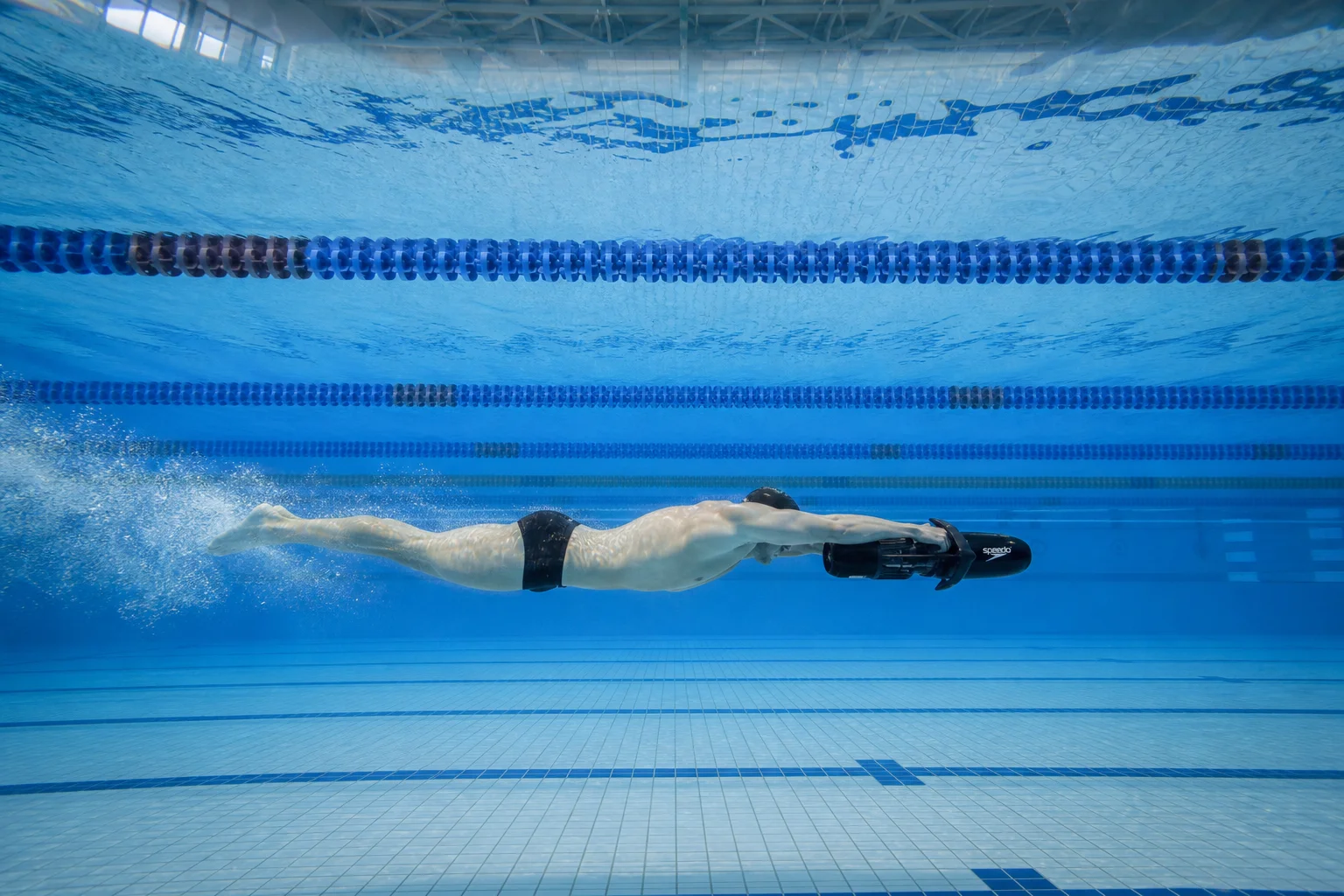 Swimmer using underwater scooter in 25-meter pool with clear water and lane markers