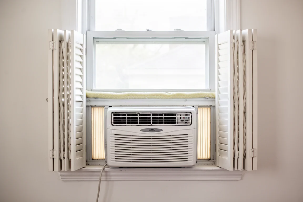 Traditionelles Fenster-Klimagerät in einem Flügelfenster montiert, mit ausgefahrenen Schallschutzklappen