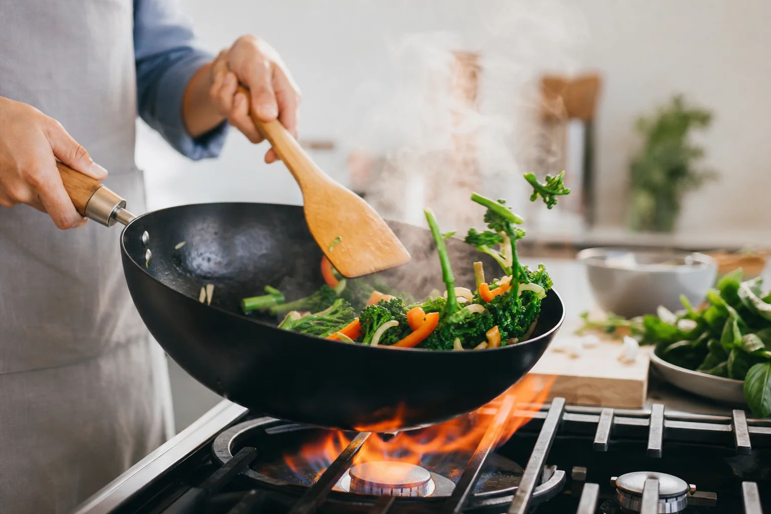 Home cook stir-frying vegetables in a wok over high heat with steam rising