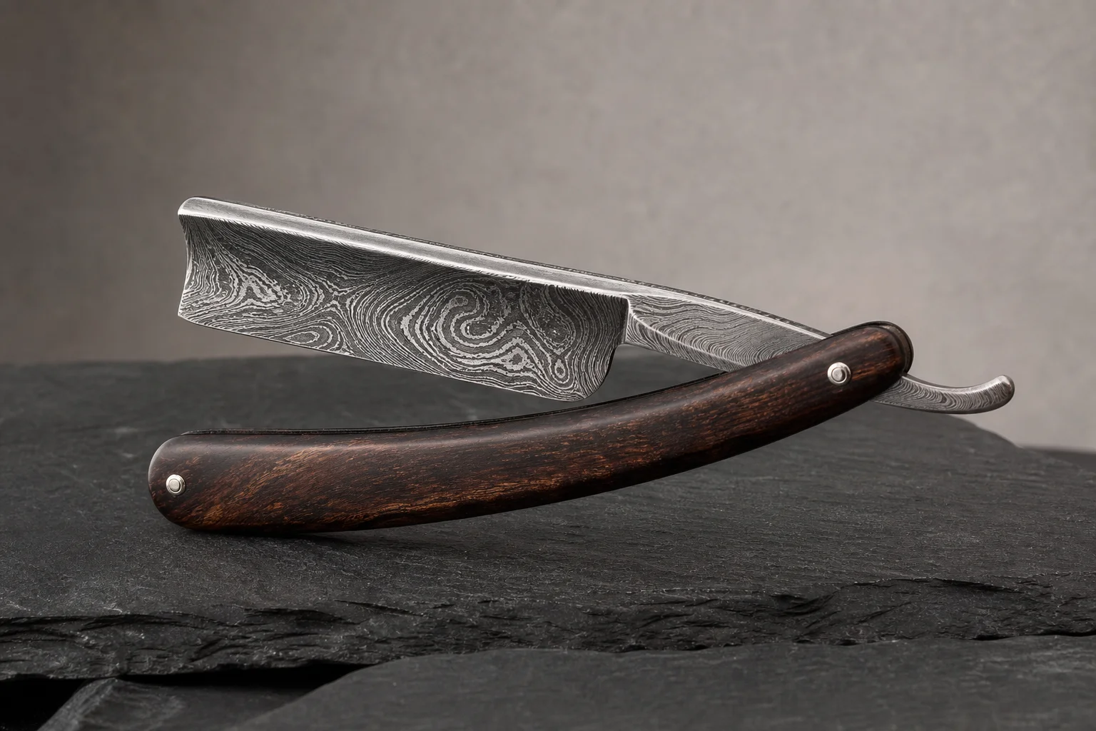 Premium folding knives with titanium handles and Damasteel blades on a dark slate surface